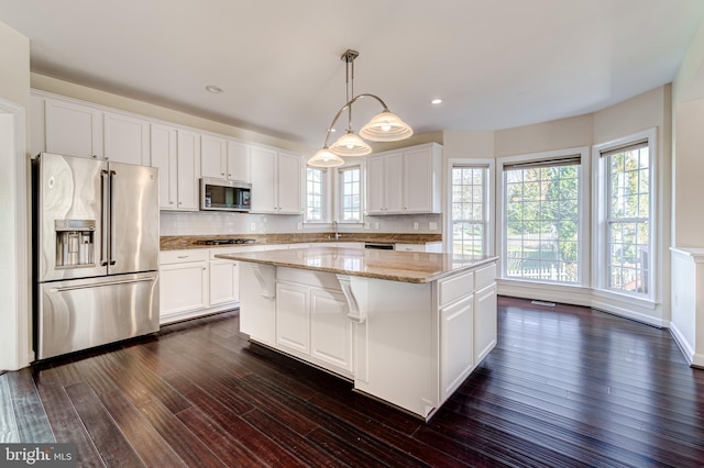 kitchen featuring stainless steel appliances, white cabinetry, hanging light fixtures, and a center island