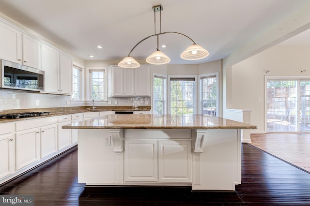 kitchen with a center island, hanging light fixtures, appliances with stainless steel finishes, light stone countertops, and white cabinets