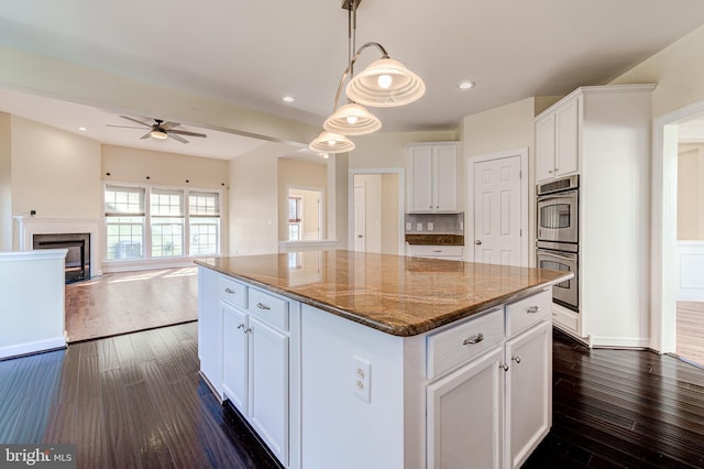 kitchen featuring stone counters, a kitchen island, decorative light fixtures, white cabinets, and dark hardwood / wood-style flooring