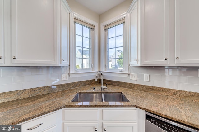 kitchen with stainless steel dishwasher, dark stone countertops, sink, and white cabinets