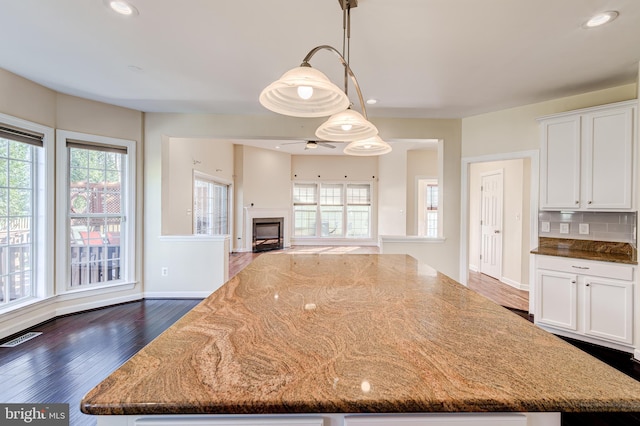 kitchen featuring a kitchen island, dark hardwood / wood-style floors, decorative light fixtures, white cabinetry, and dark stone counters