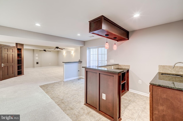 kitchen with sink, dark stone countertops, hanging light fixtures, kitchen peninsula, and light carpet