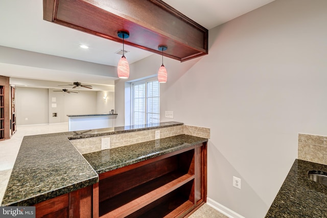 kitchen with ceiling fan, dark stone counters, and decorative light fixtures