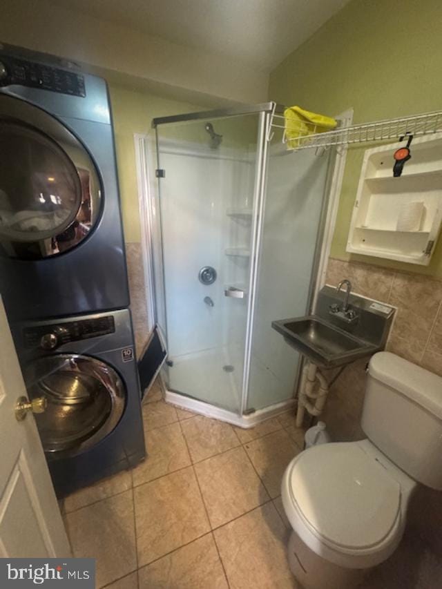 bathroom featuring sink, a shower with door, stacked washer and clothes dryer, tile patterned floors, and toilet