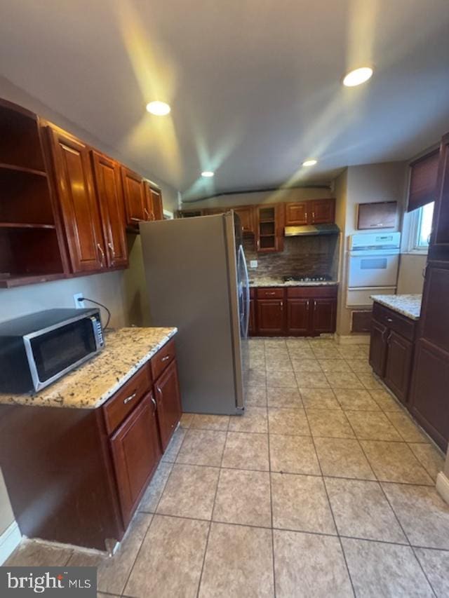 kitchen featuring light tile patterned flooring, appliances with stainless steel finishes, light stone counters, and decorative backsplash