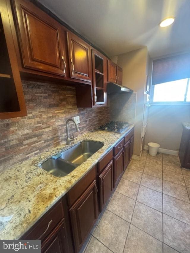 kitchen featuring light tile patterned flooring, sink, tasteful backsplash, light stone counters, and stainless steel gas stovetop