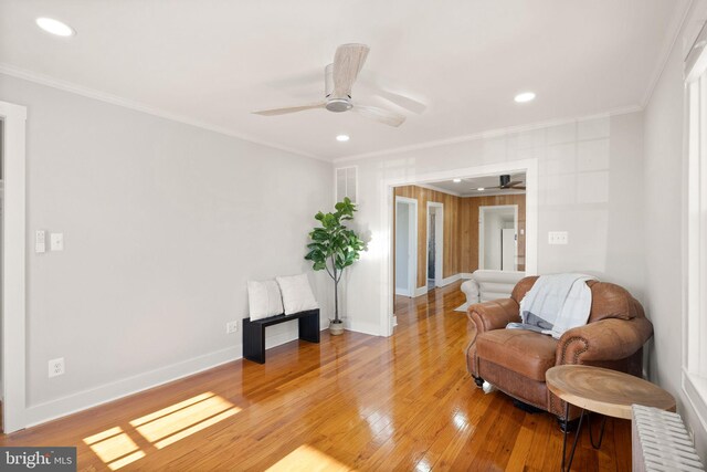 living area featuring hardwood / wood-style flooring, ceiling fan, and crown molding