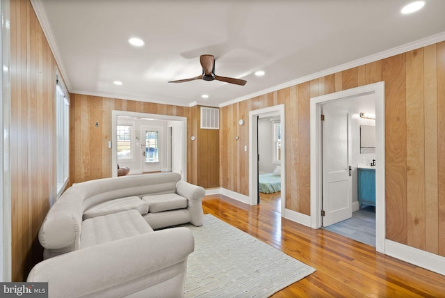 bedroom with hardwood / wood-style floors, wooden walls, ornamental molding, and ceiling fan