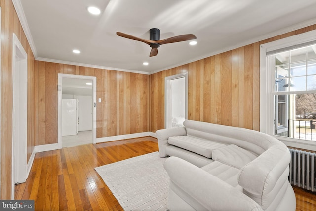 living room with ornamental molding, wooden walls, radiator, hardwood / wood-style flooring, and ceiling fan