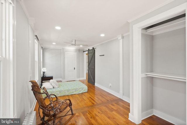 sitting room with ceiling fan, ornamental molding, a barn door, and hardwood / wood-style floors