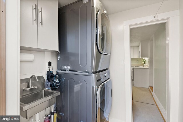 clothes washing area featuring cabinets, stacked washing maching and dryer, and sink