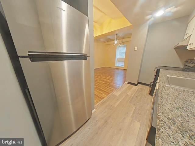 kitchen with sink, stainless steel refrigerator, white cabinetry, light stone countertops, and light wood-type flooring
