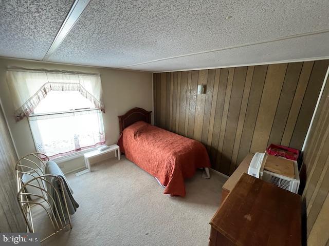 carpeted bedroom with a textured ceiling and wood walls