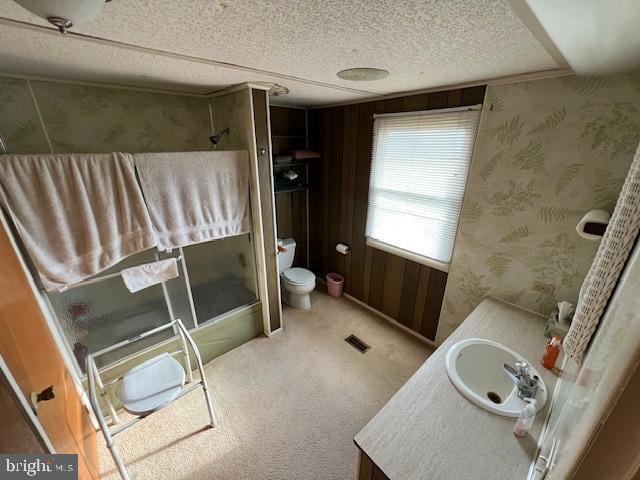 bathroom with wooden walls, vanity, a textured ceiling, toilet, and walk in shower