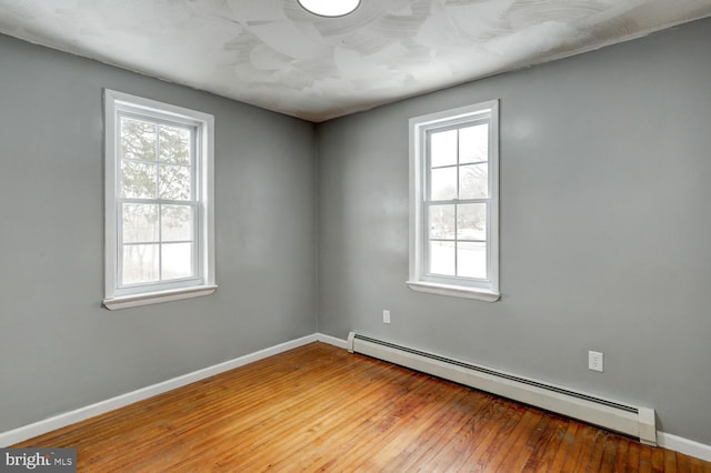 empty room featuring wood-type flooring and a baseboard heating unit