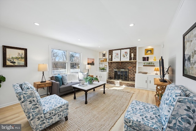 living room with ornamental molding, a brick fireplace, light wood-type flooring, and built in shelves