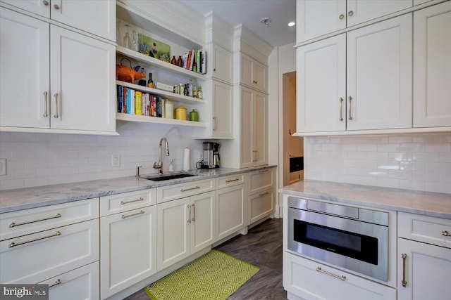 kitchen with light stone counters, dark wood-style floors, open shelves, a sink, and stainless steel microwave