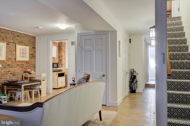 living area with brick wall, crown molding, baseboards, stairway, and brick floor