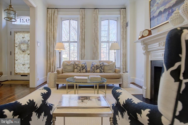 living room featuring baseboards, a chandelier, a fireplace with flush hearth, ornamental molding, and wood finished floors