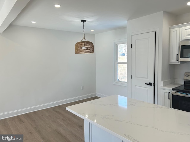 kitchen featuring hardwood / wood-style flooring, appliances with stainless steel finishes, white cabinetry, hanging light fixtures, and light stone countertops