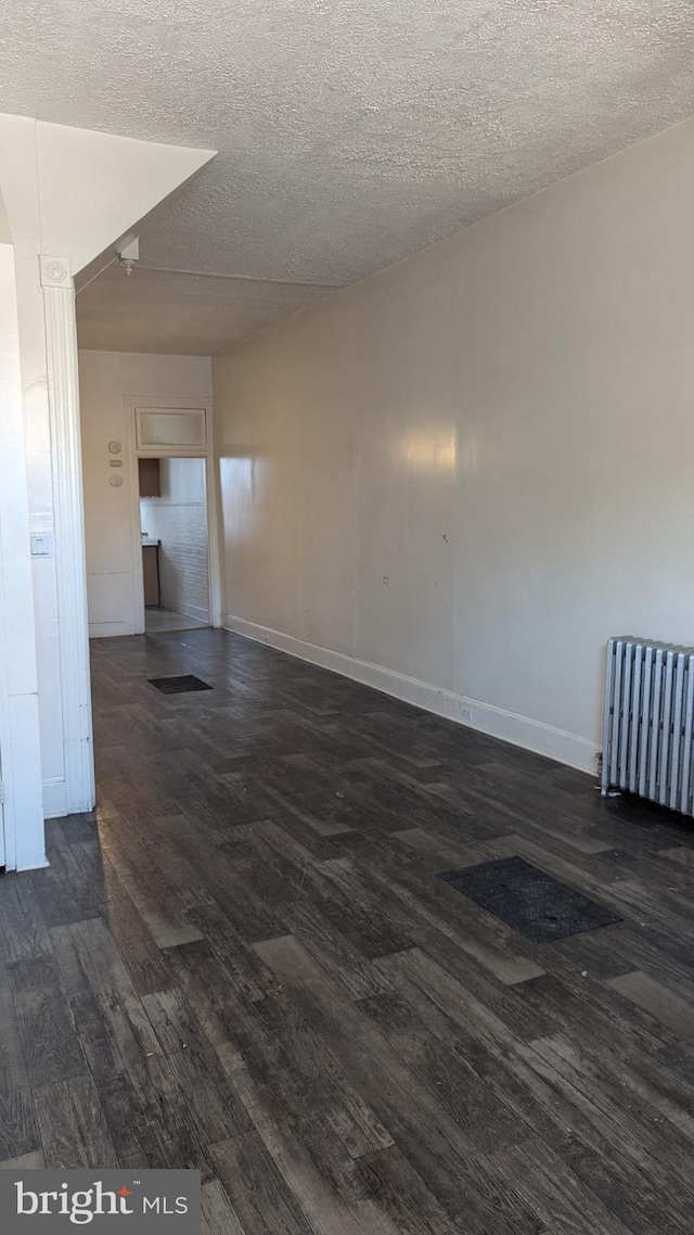 spare room with dark wood-type flooring, radiator heating unit, and a textured ceiling