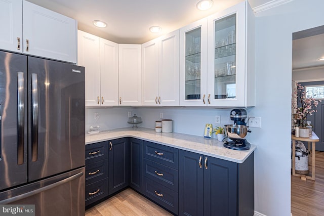 kitchen with white cabinets, light stone counters, stainless steel fridge, and light hardwood / wood-style floors