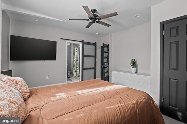 bedroom with ceiling fan, a barn door, and ensuite bath