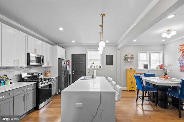 kitchen featuring sink, appliances with stainless steel finishes, a wealth of natural light, a center island with sink, and decorative light fixtures