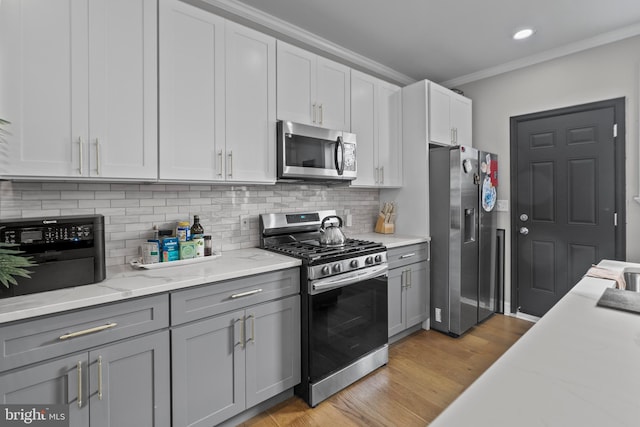 kitchen with light hardwood / wood-style flooring, ornamental molding, gray cabinets, and stainless steel appliances