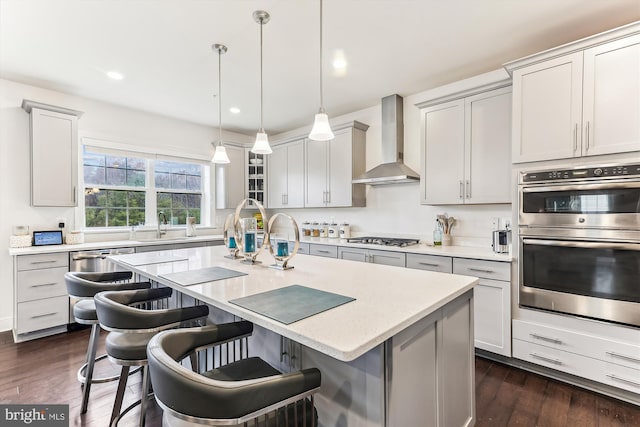 kitchen with appliances with stainless steel finishes, dark hardwood / wood-style floors, pendant lighting, a breakfast bar area, and wall chimney exhaust hood