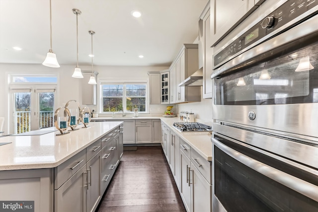 kitchen with appliances with stainless steel finishes, decorative light fixtures, light stone countertops, and gray cabinetry