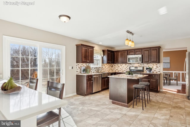 kitchen with dark brown cabinetry, hanging light fixtures, a kitchen island, stainless steel appliances, and backsplash