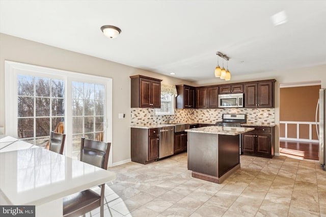 kitchen with appliances with stainless steel finishes, tasteful backsplash, dark brown cabinetry, a kitchen island, and decorative light fixtures