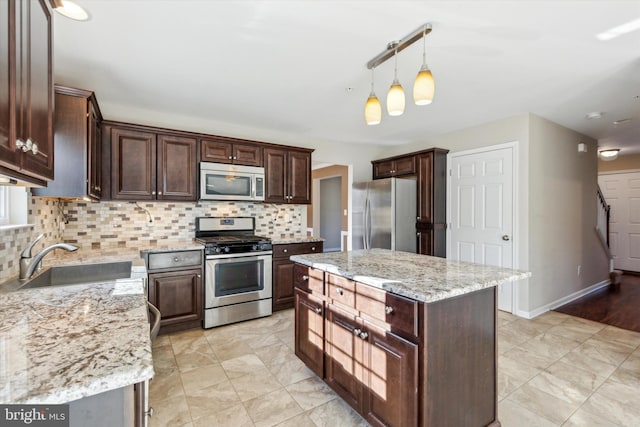 kitchen featuring a kitchen island, appliances with stainless steel finishes, sink, hanging light fixtures, and light stone counters