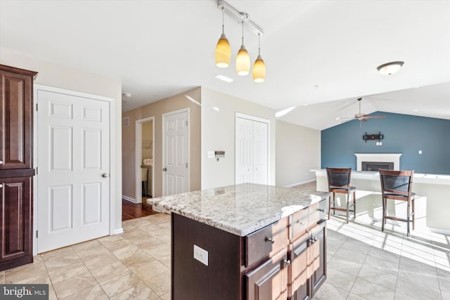 kitchen with lofted ceiling, a center island, pendant lighting, ceiling fan, and light stone countertops