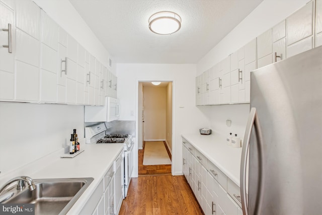 kitchen with sink, white cabinetry, a textured ceiling, white appliances, and light hardwood / wood-style floors