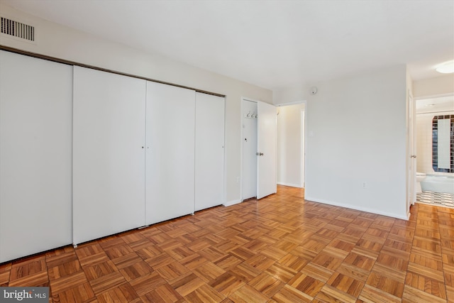 unfurnished bedroom featuring light parquet floors, ensuite bath, and a closet