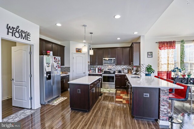 kitchen featuring dark brown cabinetry, a center island, hanging light fixtures, appliances with stainless steel finishes, and kitchen peninsula