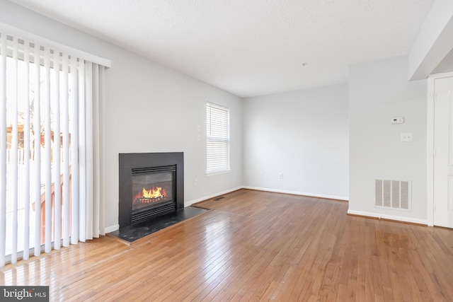 unfurnished living room featuring light wood-style floors, baseboards, visible vents, and a glass covered fireplace