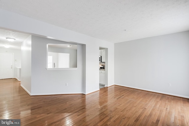 unfurnished room with a textured ceiling, baseboards, and wood finished floors