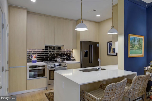 kitchen with tasteful backsplash, a breakfast bar area, appliances with stainless steel finishes, light wood-style floors, and a sink