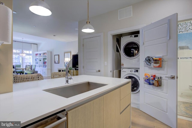 laundry room featuring stacked washer and dryer, laundry area, a sink, visible vents, and light wood finished floors