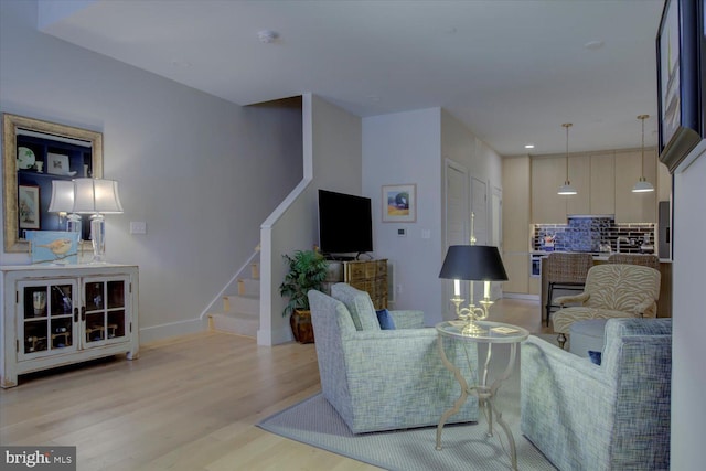 living room featuring baseboards, light wood finished floors, and stairs