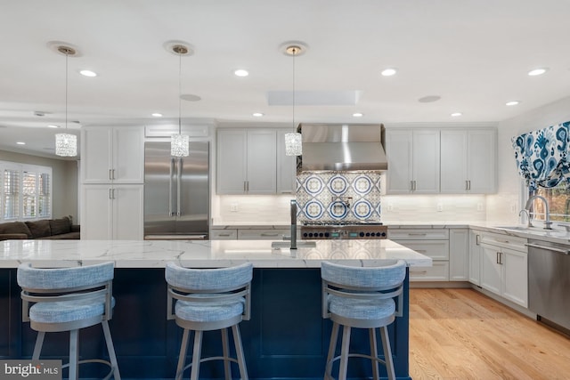 kitchen with wall chimney range hood, decorative light fixtures, stainless steel appliances, and sink