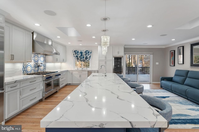 kitchen featuring light stone counters, wall chimney exhaust hood, range with two ovens, and a large island with sink