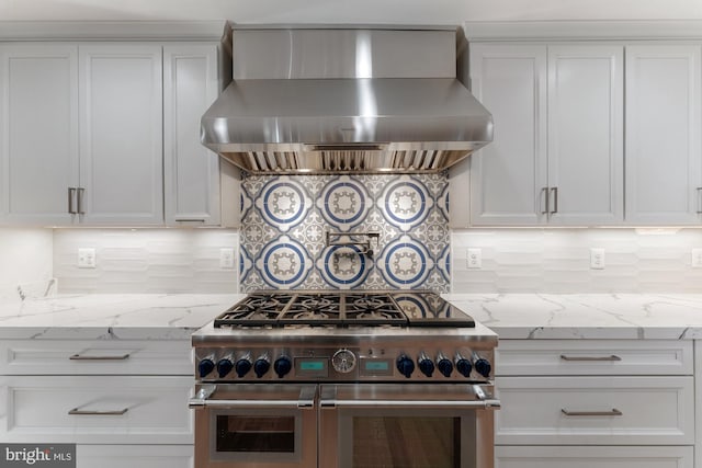 kitchen with light stone counters, double oven range, wall chimney range hood, and white cabinets