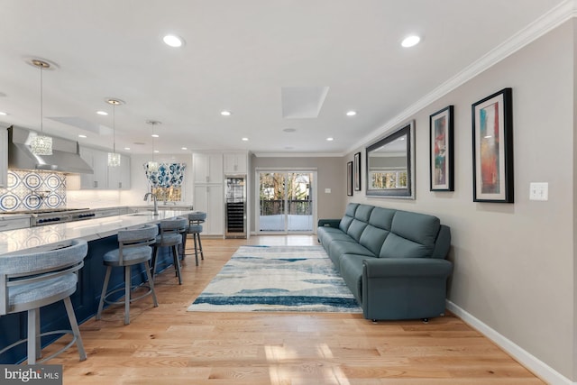 living room featuring sink, ornamental molding, light hardwood / wood-style floors, and beverage cooler