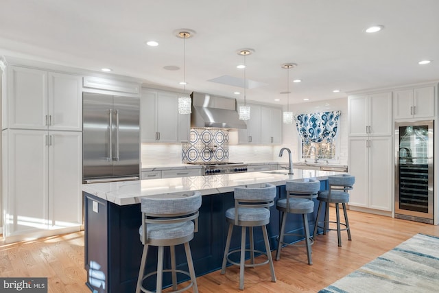 kitchen with a large island with sink, beverage cooler, wall chimney exhaust hood, and stainless steel built in fridge