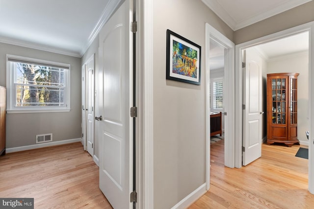 corridor with ornamental molding and light hardwood / wood-style flooring