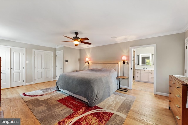 bedroom featuring sink, ornamental molding, light hardwood / wood-style floors, and multiple closets